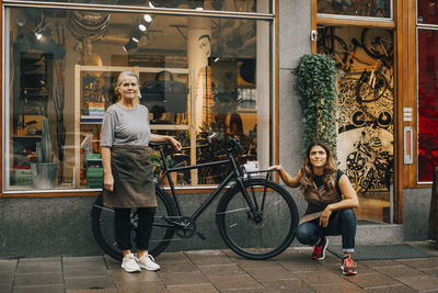 Full length portrait of smiling young woman sitting at store