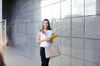 Portrait of businesswoman holding documents while standing against wall