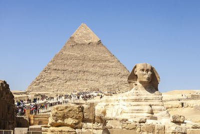 Tourists at the sphinx and pyramid of chephren against clear blue sky