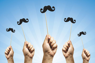Multiple image of hand holding mustache prop against blue background