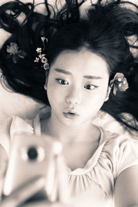 High angle view of woman with long hair taking selfie while lying down on bed