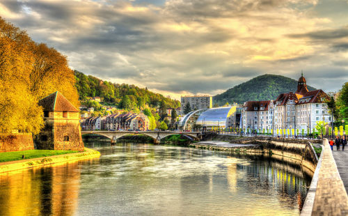 Arch bridge over river by buildings against sky