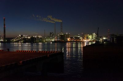 Illuminated city by sea against sky at night