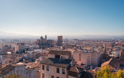 Drone view of residential buildings and trees located on streets of granada against cloudless blue sky in autumn in spain