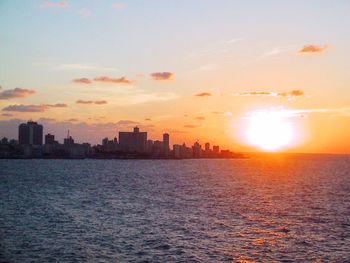 Sea by cityscape against sky during sunset