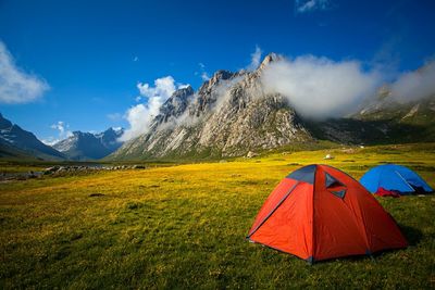 Tents on grassy field by mountain against sky