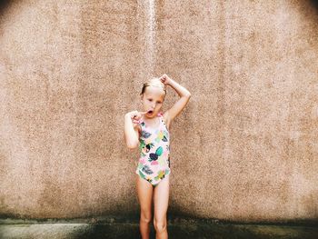 Girl wearing swimwear while taking shower against wall