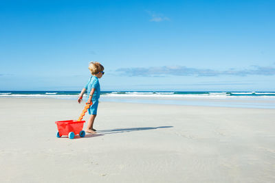 Rear view of woman standing at beach against blue sky