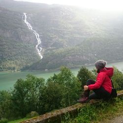 Side view of man sitting on mountain against sky