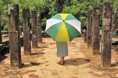Woman with umbrella walking on footpath against trees
