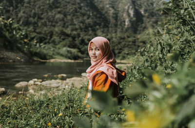 Portrait of young woman looking away against plants