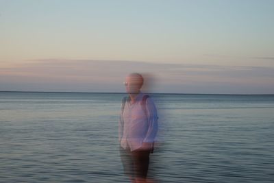 Double exposure of man standing on shore against sky during sunset