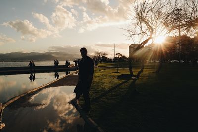 Silhouette man standing on lakeshore against sky