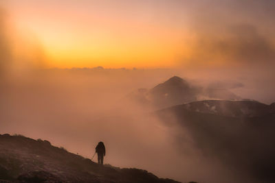 Rear view of silhouette man standing on mountain against sky during sunset