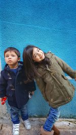 Siblings standing against blue wall