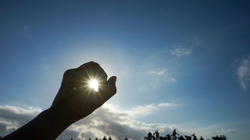 Low angle view of sunlight streaming through hand against sky