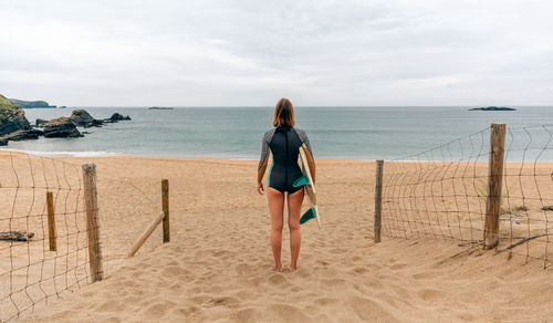 Surfer woman with wetsuit and surfboard looking at the sea