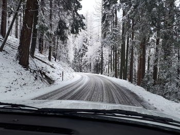 Road amidst trees seen through car windshield during winter