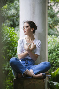 Young woman looking away while sitting outdoors