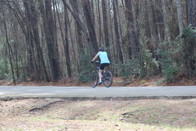 Woman riding bicycle on road against trees