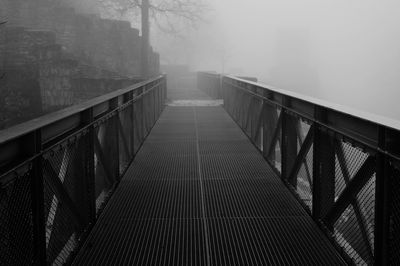 Footbridge in foggy weather against sky during winter