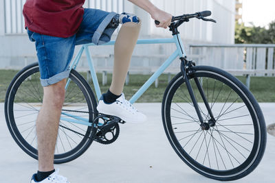 Young male with disability and prosthetic leg riding bicycle on street