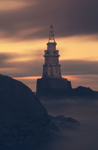 Low angle view of lighthouse by building against sky during sunset