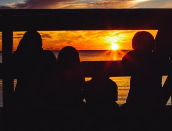 Silhouette people in sea against sky during sunset