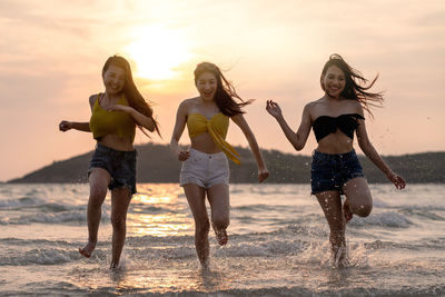 Smiling friends running in sea against sky