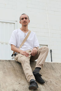 Portrait of young man sitting against wall