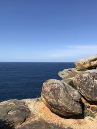 Rocks by sea against clear blue sky