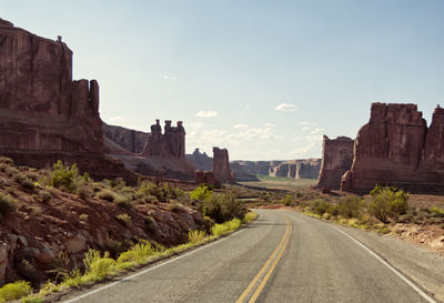 Road leading towards rock formations against sky