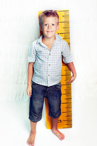 Portrait of smiling boy standing with tape measure standing against wall