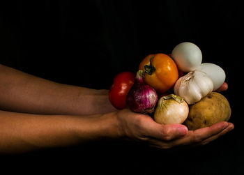 Close-up of hand holding fruits against black background
