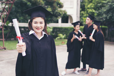 Cheerful student in graduation gown standing outdoors