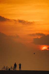 Silhouette man with bicycle by sea against orange sky