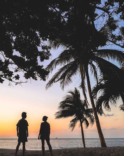 Silhouette people on beach against sky during sunset