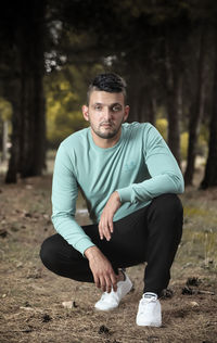 Portrait of young man crouching against trees