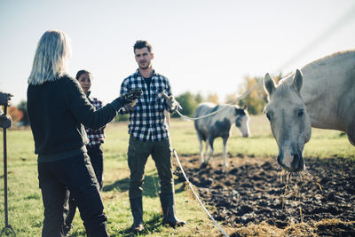 Mid adult man talking with instructor by horse at organic farm