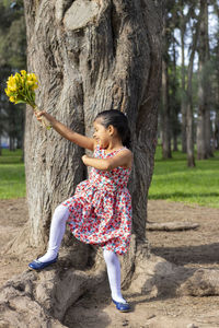 Full length of smiling girl by tree trunk