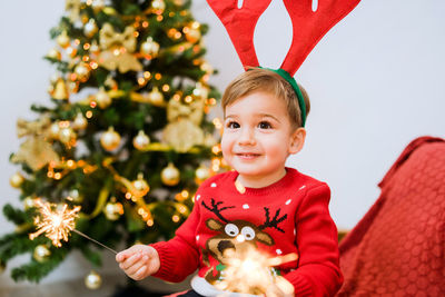 Cute boy holding sparkler against christmas tree at home