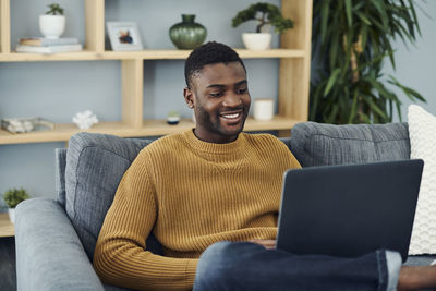 Young man using mobile phone while sitting on sofa at home