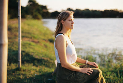 Woman looking away while sitting at lakeshore