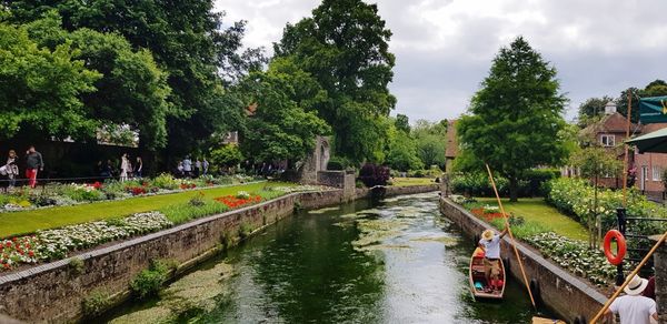 People on canal by trees against sky