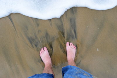 Low section of man standing at sea shore