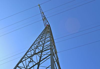 Low angle view of electricity pylon against clear blue sky