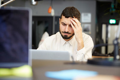 Stressed male entrepreneur looking at laptop while sitting in office