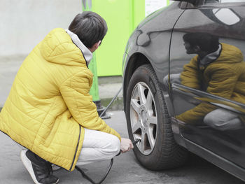 Young caucasian man in a yellow jacket and gray sweatpants, squatting pumping a tire