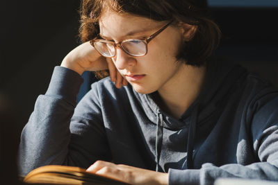 Close up of young girl at table reading book with serious face