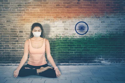 Portrait of woman sitting against brick wall